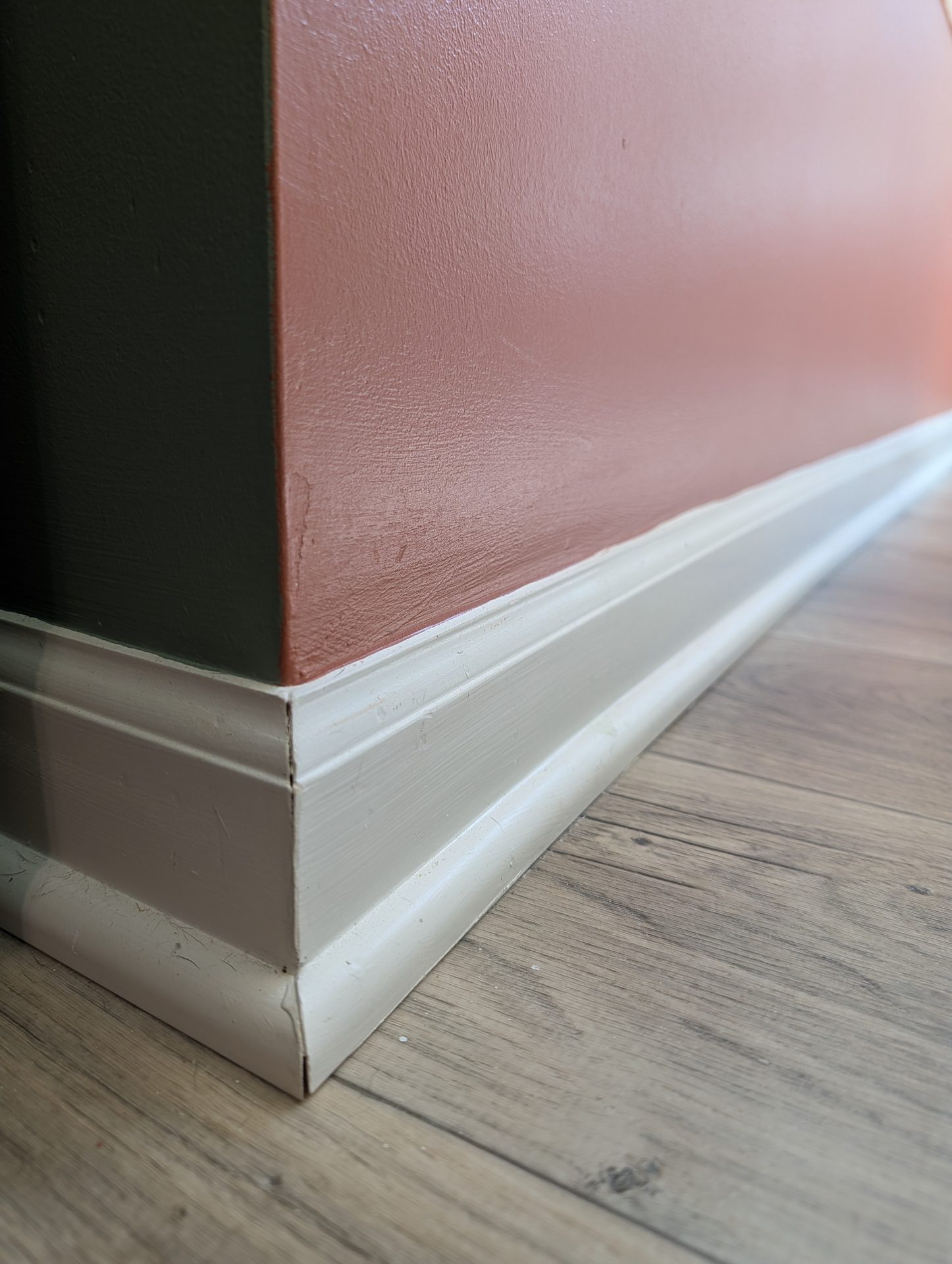 Cut line where terracotta and dark green walls meet a painted baseboard