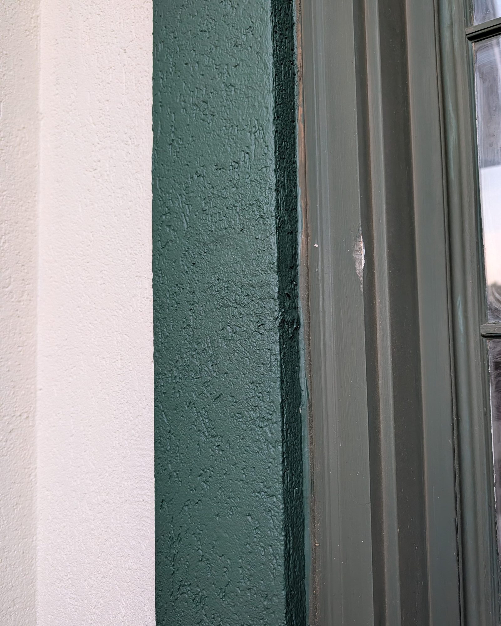 After: the stucco patched and repainted dark green, window trim repainted